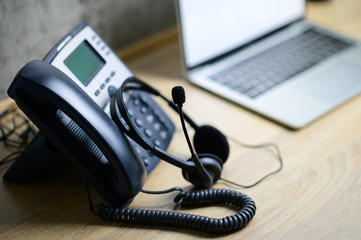 IP telephone with headset and laptop computer on wood table, office work space