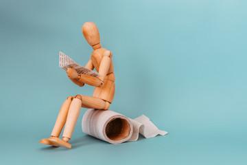 Wooden figure sit on a roll of toilet paper and reading the newspaper
