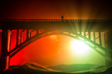 Artwork decoration. Silhouette of powerful metallic bridge at night with foggy backlight. Silhouette of person standing on bridge.