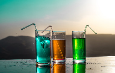 Cooling summer drink concept. Cocktail glasses splashing on sunset. Close up wet glass of cold drink on the terrace.