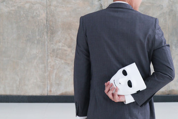 Businessman holding white mask in his hand dishonest cheating agreement.Faking and betray business partnership concept