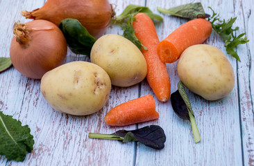 Ripe carrots, potato, garlic, salad leafs and brown onion on wooden table background. Cooking ingredients. Harvest