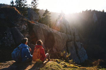 couple hikers with backpacks are sitting on edge of slope and enjoying a beautiful morning...