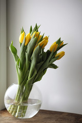 A bouquet of yellow tulips in a vase on the windowsill. A gift to a woman's day from yellow tulip flowers. Beautiful yellow flowers in a vase by window.