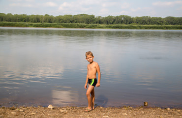 portrait of a seven-year-old boy standing on the bank of a river on a hot summer day © vitec40