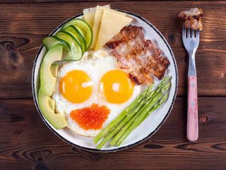 Top view of ketogenic diet breakfast on the white plate with a fork on dark wooden background.