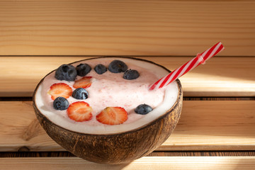 View of strawberry smoothie in a coconut bowl with blueberries on a wooden background. Soft focus.
