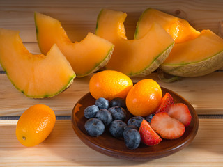 Close up view of blueberries and strawberries and melon and kumquat on a wooden background illuminated by sunlight. Soft focus.