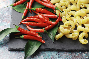 Uncooked pasta on a stone background. With seasonings and spices, spicy chili peppers.