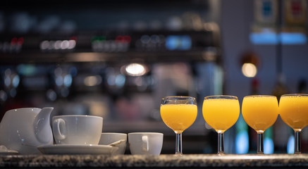 Glasses of orange juice, a teapot and two coffee cups on a bar counter