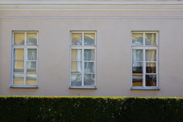 Wall with three windows on the background of green bushes