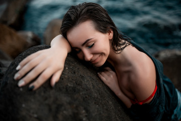 Beautiful girl in a black shirt and red bra is lying on a stone against the background of the sea