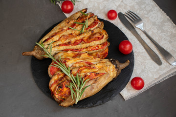 Dietary fan of eggplant white filled with tomatoes and cheese. Nearby are cherry tomatoes, rosemary branches. It is worth soy sauce and metal appliances. On a dark background.