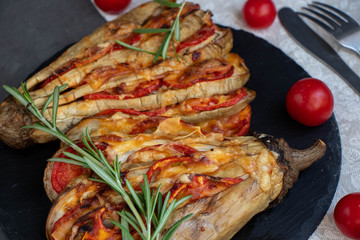Dietary fan of eggplant white filled with tomatoes and cheese. Nearby are cherry tomatoes, rosemary branches. It is worth soy sauce and metal appliances. On a dark background.