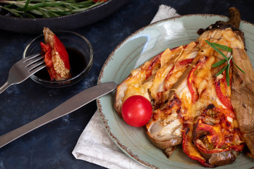 Dietary fan of eggplant white filled with tomatoes and cheese. Nearby are cherry tomatoes, rosemary branches. It is worth soy sauce and metal appliances. On a dark background.
