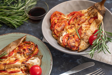 Dietary fan of eggplant white filled with tomatoes and cheese. Nearby are cherry tomatoes, rosemary branches. It is worth soy sauce and metal appliances. On a dark background.