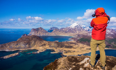 Offersoykammen Hiking Trail, Vestvagoy, Lofoten Islands, Norway. Top view from the peak of the mountain. Man taking photo of panorama view of fjords with blue water