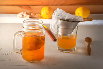 Homemade fermented drink Kombucha in a glass jar with lemon and ginger on a wooden table.