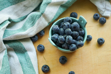 selective focus, Blueberry berries in a clay white small bowl on a light wooden Board with a light green striped cloth kitchen napkin