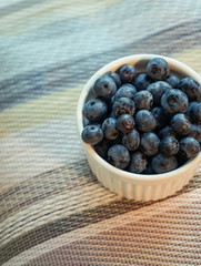 Blueberries in white clay small bowl on the background of linen with bright fabrics and knitted of twine tablecloths