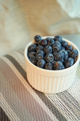 Blueberries in white clay small bowl on the background of linen with bright fabrics and knitted of twine tablecloths