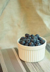 Blueberries in white clay small bowl on the background of linen with bright fabrics and knitted of twine tablecloths
