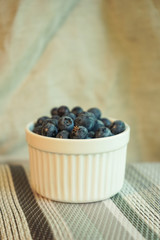 Blueberries in white clay small bowl on the background of linen with bright fabrics and knitted of twine tablecloths