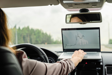 Business woman turn on car emergency stop button driving on the highway and working using laptop.