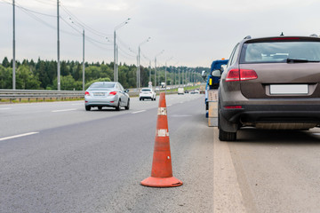 Attention traffic cone on the road. Selective focus. Tow truck towing a broken down car on the highway
