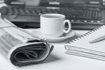 Newspaper on the desk, laptop, cup of coffee.