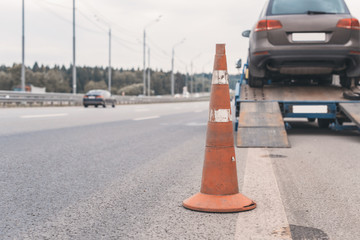 Attention traffic cone on the road. Selective focus. Tow truck towing a broken down car on the...