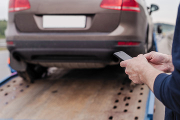 Man with mobile phone.Tow truck with worker towing a broken down car on the highway. Selective focus. Concept