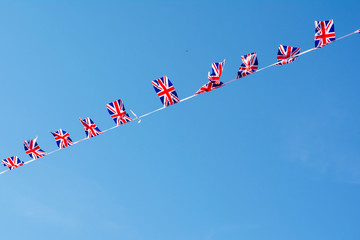 A row of small flags of Britain fluttering in the wind against the background of a deep blue sky.