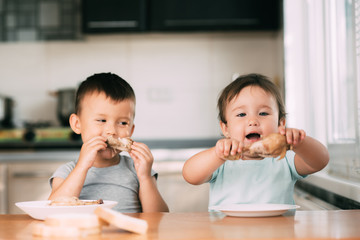 Kids boy and girl , brother and sister in the kitchen having fun and eating chicken with appetite