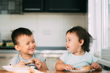 Kids boy and girl , brother and sister in the kitchen having fun and eating chicken with appetite