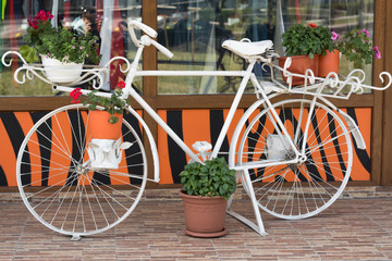 Fototapeta na wymiar Decorative, vintage bike, painted white, used as a stand for flowerpots. stands in the city center