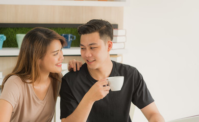 Young happy Asian couple eating breakfast and using laptop in the modern kitchen room, Romance sweet couple