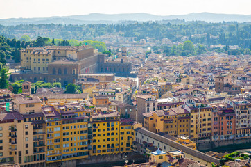 Top aerial panoramic view of Florence city, Ponte Vecchio bridge over Arno river, Palazzo Pitti palace, buildings houses with orange red tiled roofs, blue sky white clouds, Tuscany, Italy