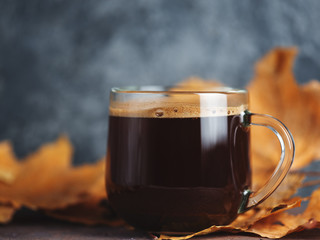 Glass espresso coffee Cup with autumn dry leaves on the background. Cold season with hot coffee
