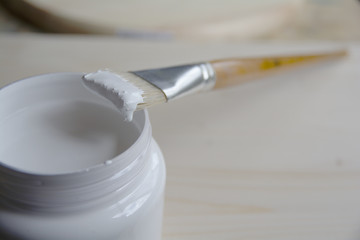 Plastic can with white acrylic primer and a bristle brush on a wooden panel. Preparing the surface...