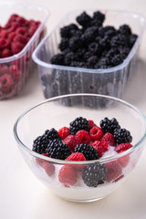 Ice cream with raspberry, blackberry in glass bowl near two containers of berries on white background