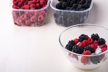 Ice cream with raspberry, blackberry in glass bowl near two containers of berries on white background
