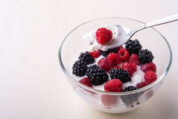 Ice cream with raspberry, blackberry berries with spoon in glass bowl on white background