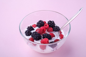 Ice cream with raspberry, blackberry berries with spoon in glass bowl on pink background