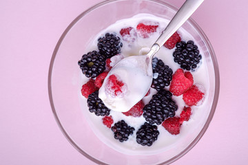Ice cream with raspberry, blackberry berries with spoon in glass bowl on pink background