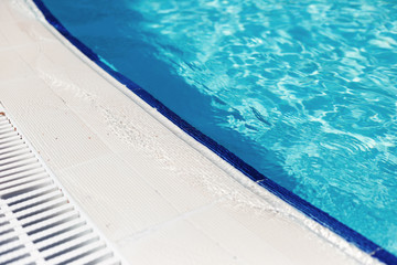 Blue water with light reflection at the edge of the curved swimming pool. The concept of summer travel and recreation