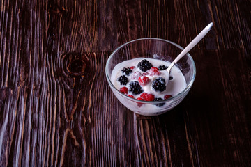 Ice cream with raspberry, blackberry berries with spoon in glass bowl on dark wooden background