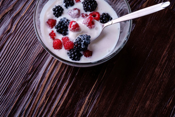 Ice cream with raspberry, blackberry berries with spoon in glass bowl on dark wooden background