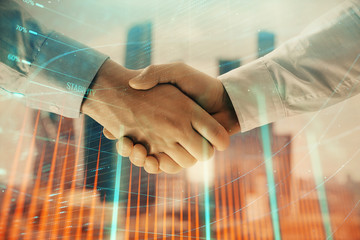Double exposure of financial graph on cityscape background with two businessman handshake. Concept of stock market deal