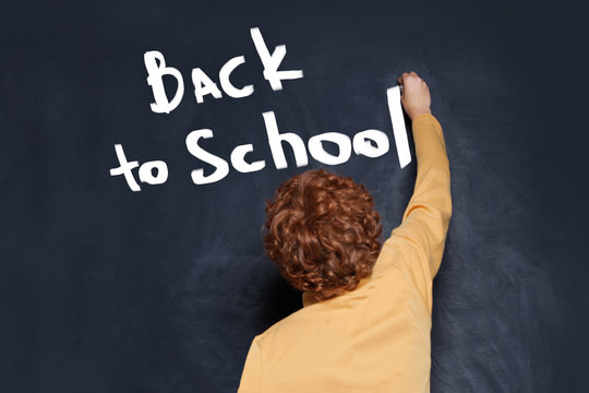 Child writing boy Back to school text on chalkboard background
